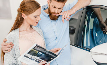 Kvinna och man står brevid en bil och tittar på en broschyr tillsammans. 